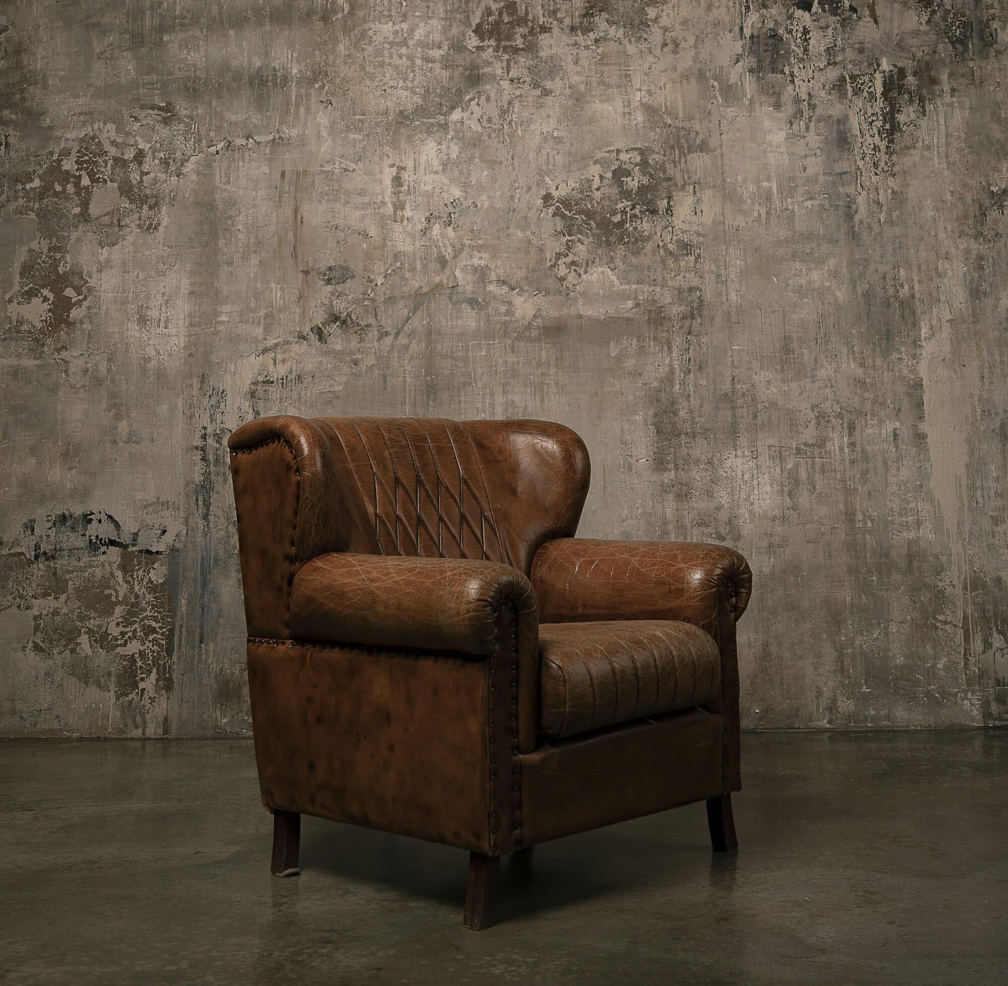 Brun läderfåtölj framför en ljus, patinerad vägg