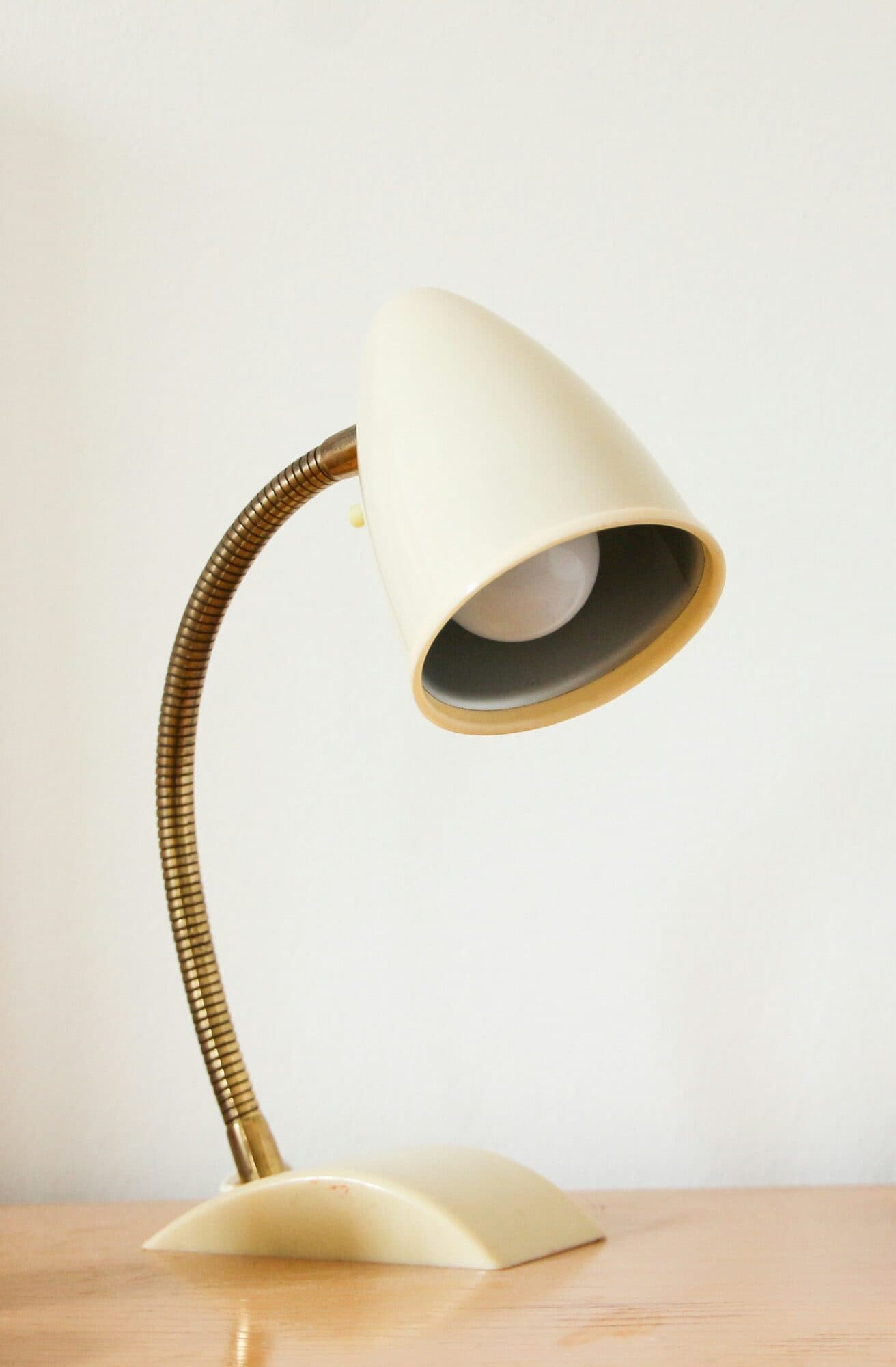 Krämvit bordslampa med böjlig mässingsarm på ett träbord